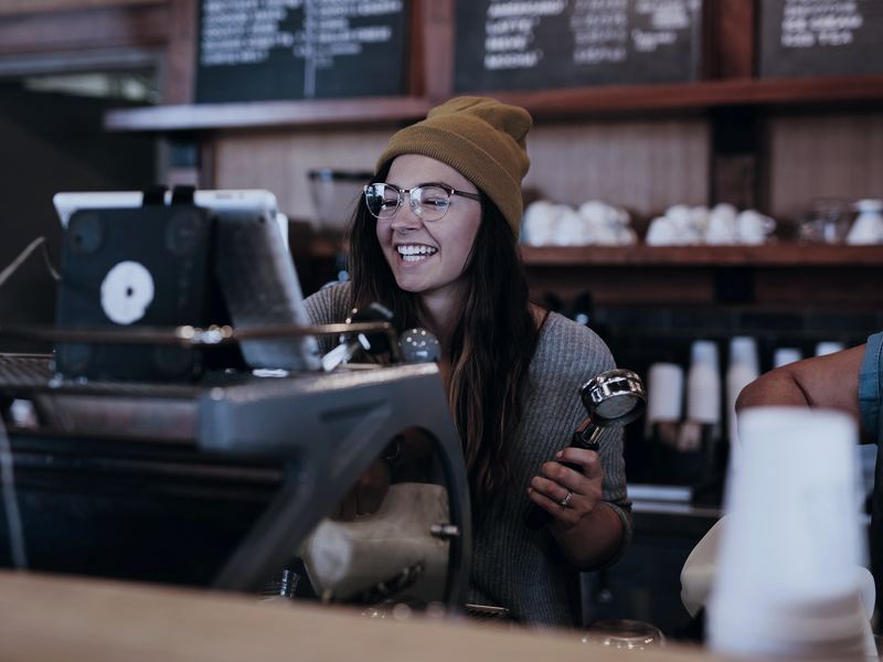 Barista laughing behind the espresso machine in a busy coffee shop