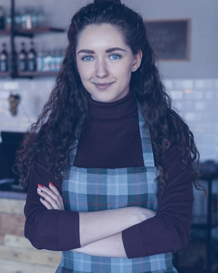 Coffee shop owner standing in front of her counter with her arms folded, smiling