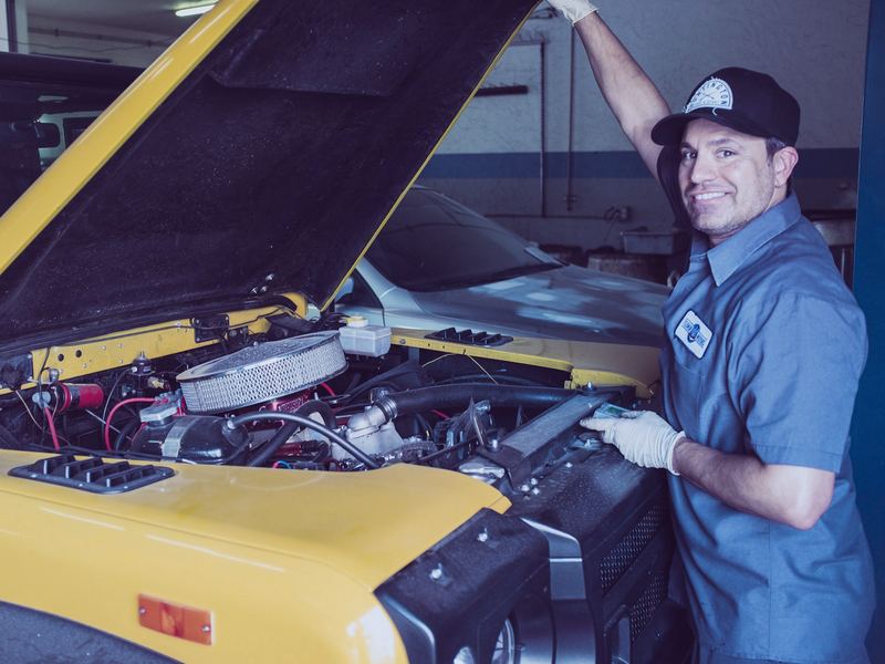 Auto technician smiling beside the open hood of a car in a repair shop